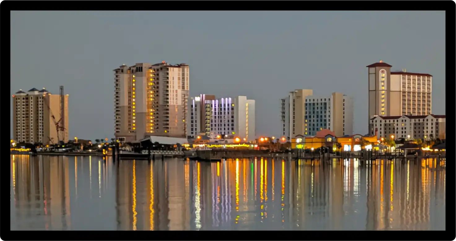 Original photograph of the Pensacola Beach waterfront skyline at dusk, with illuminated buildings reflected in calm water